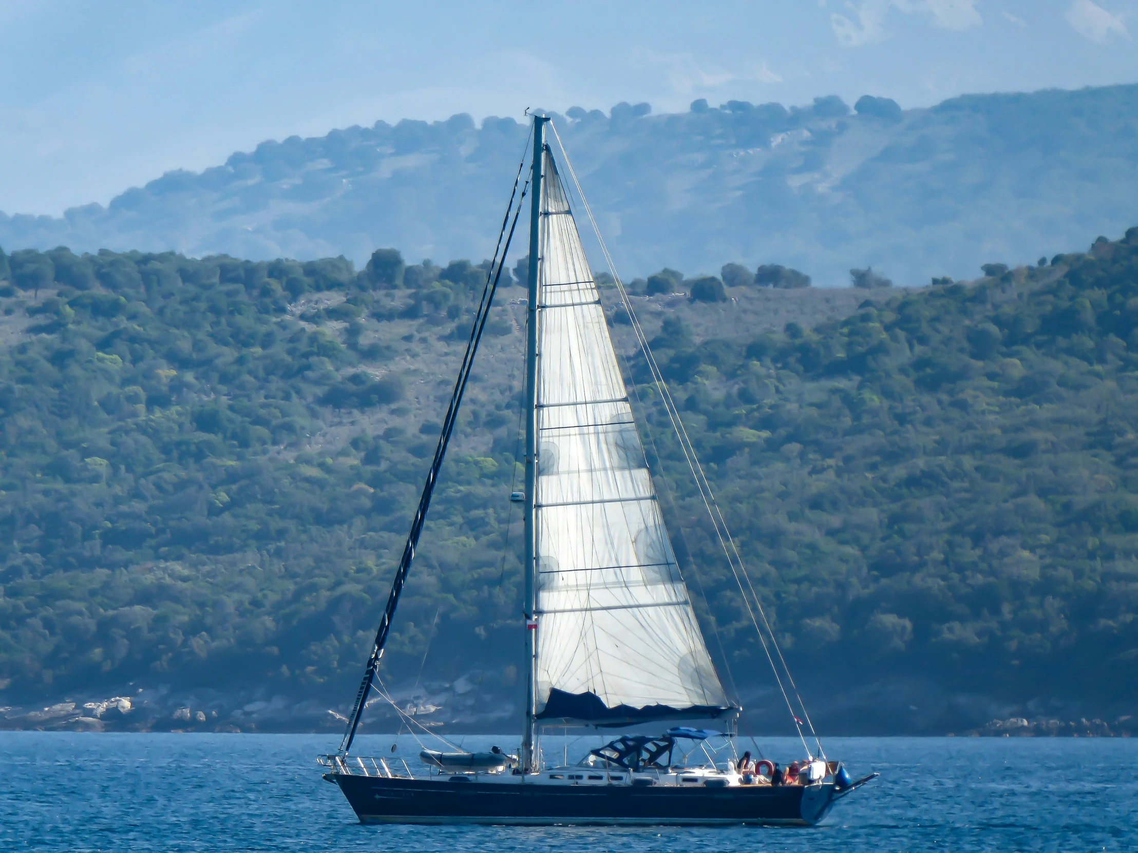 a sailboat in the water with the hills behind it