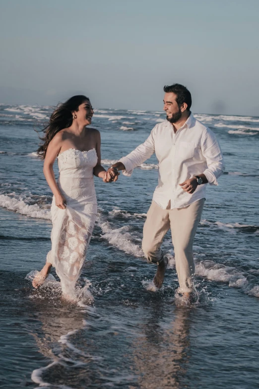 a bride and groom are walking through the ocean holding hands