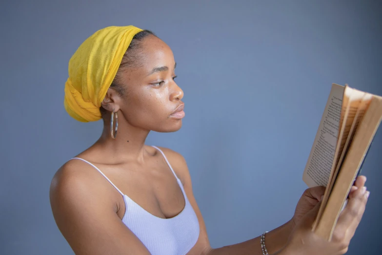 a woman in a white tank top with a yellow turban on her head reads a book