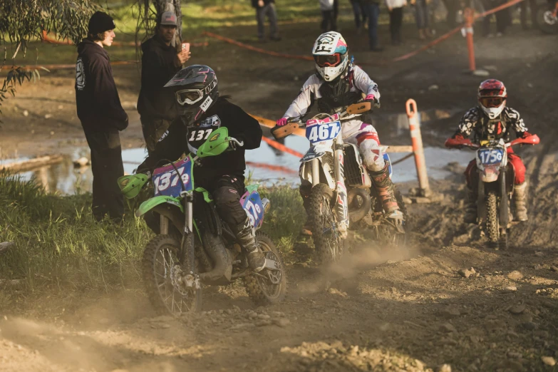 a group of young children on motorcycles racing on dirt track