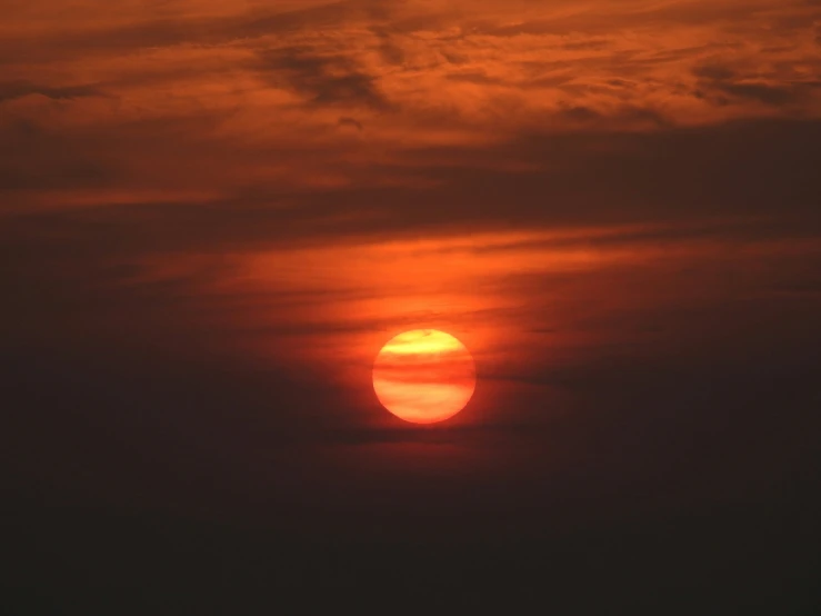 a large orange sun over the clouds in a sky