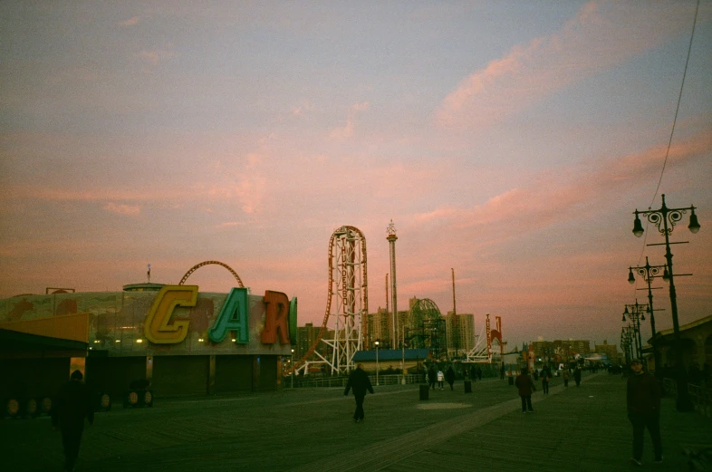 several people walking down a sidewalk next to a roller coaster