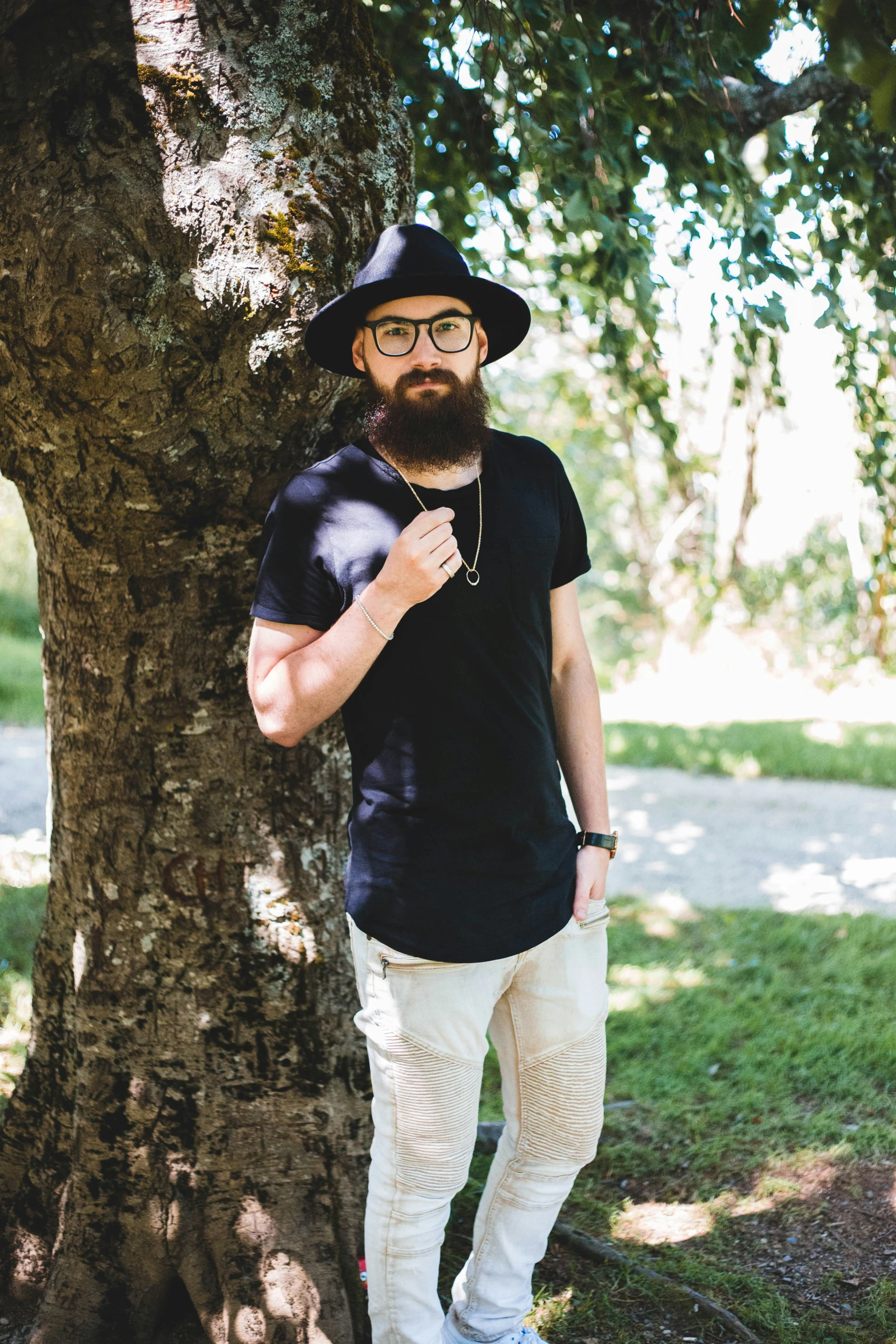 a bearded man wearing eyeglasses poses in front of a tree