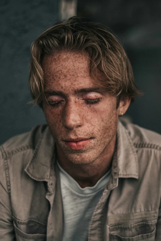 a man wearing a shirt stares down as he has his eyes covered