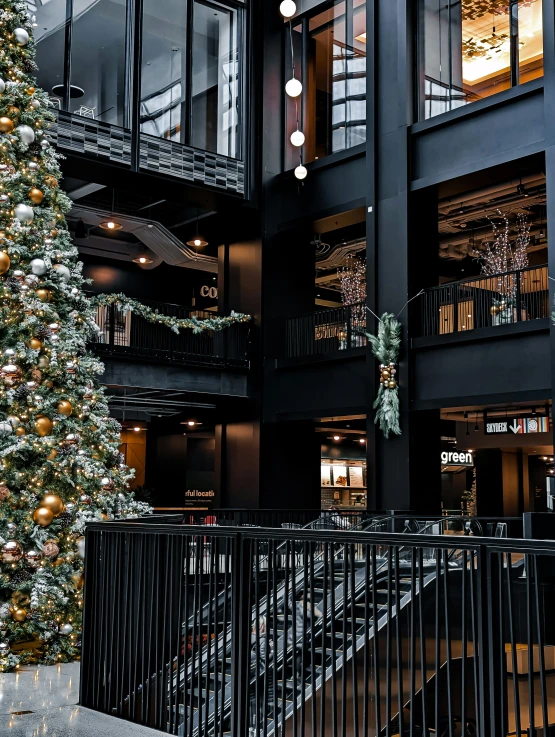 a christmas tree with lights and ornaments is next to a black railing