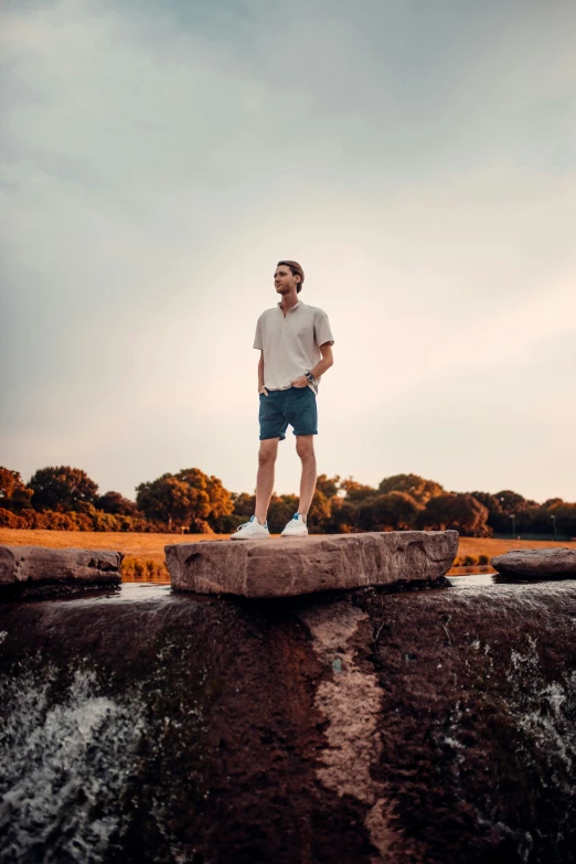 a young man standing on a rock by the water