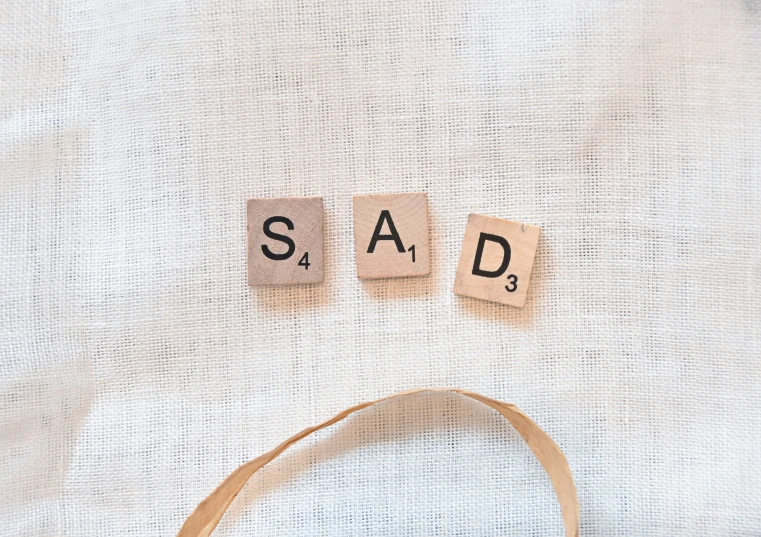 the word sad spelled with scrabble letters on wood block