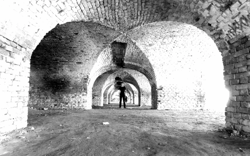 a man standing alone in a tunnel with brick walls