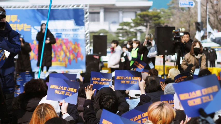 a group of people in coats and hats holding blue signs