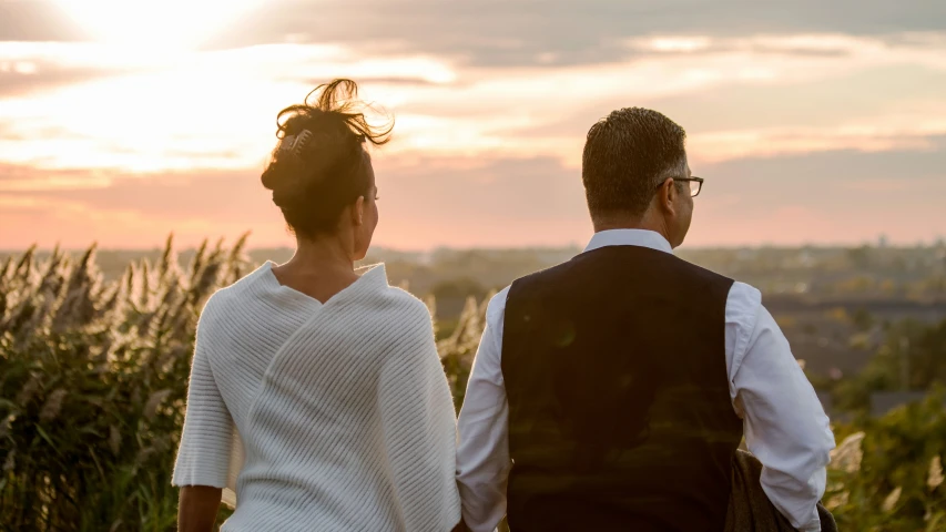 a couple standing in the grass at sunset