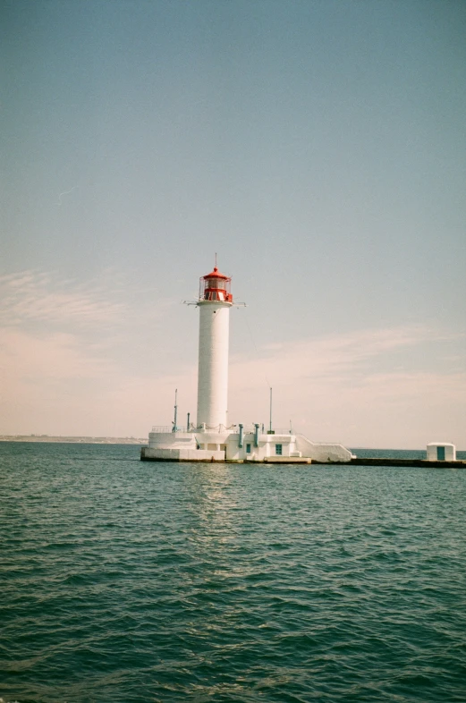 a white lighthouse with red top is in the middle of the ocean