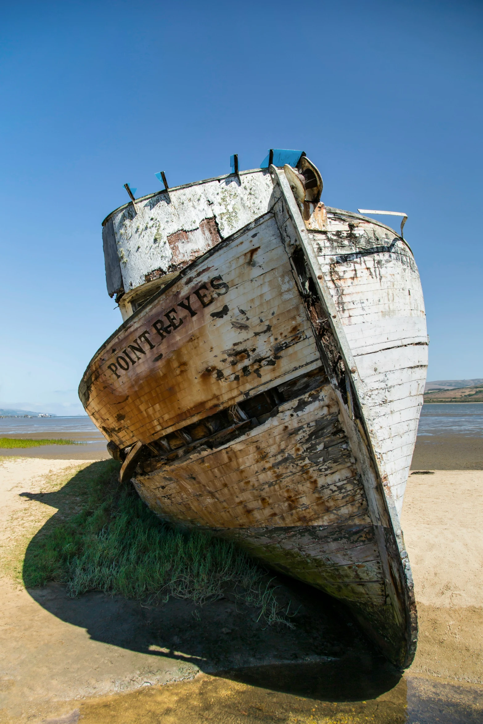 an old boat sits on the beach with grass growing all around