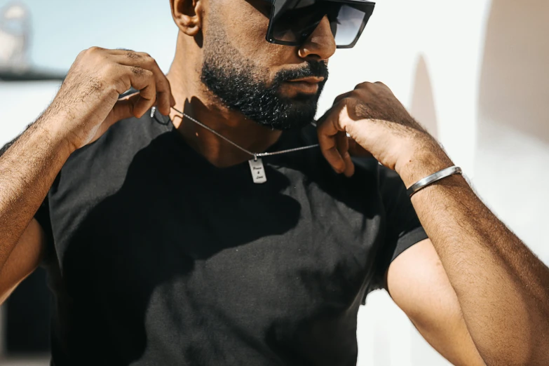 an african man adjusts his sunglasses while standing outside