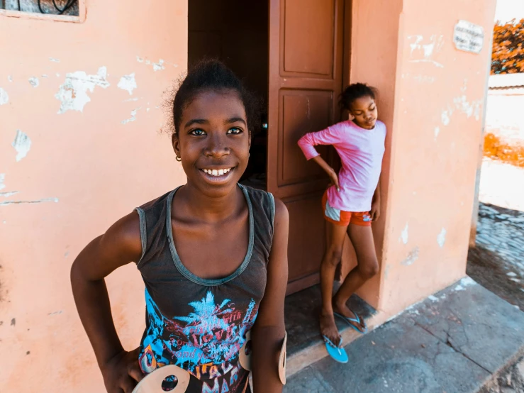 a little girl smiling next to another girl holding a surfboard