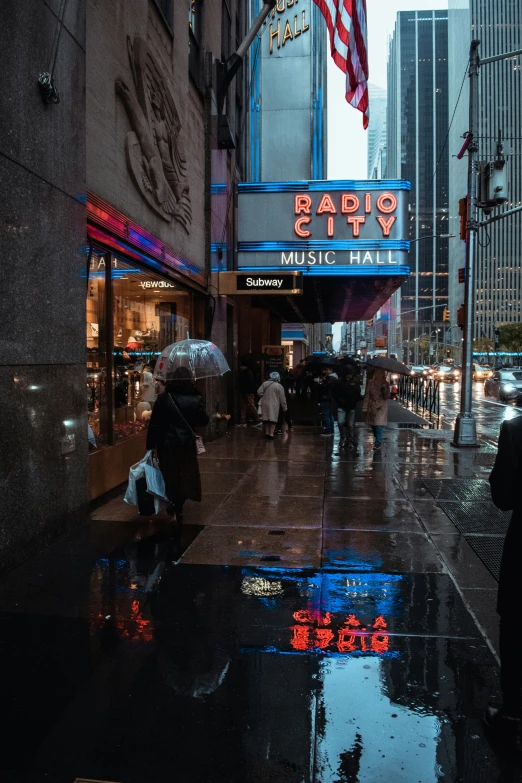 pedestrians walk down the sidewalk of an intersection in the rain