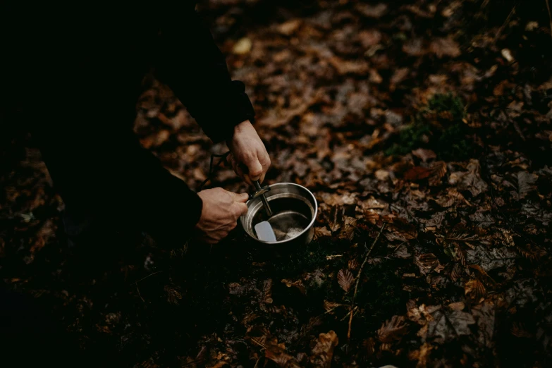 a man is bending over with his hands while holding a small bowl in the woods