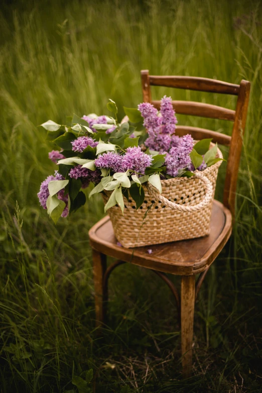 a basket filled with lots of purple flowers sitting on top of a wooden chair