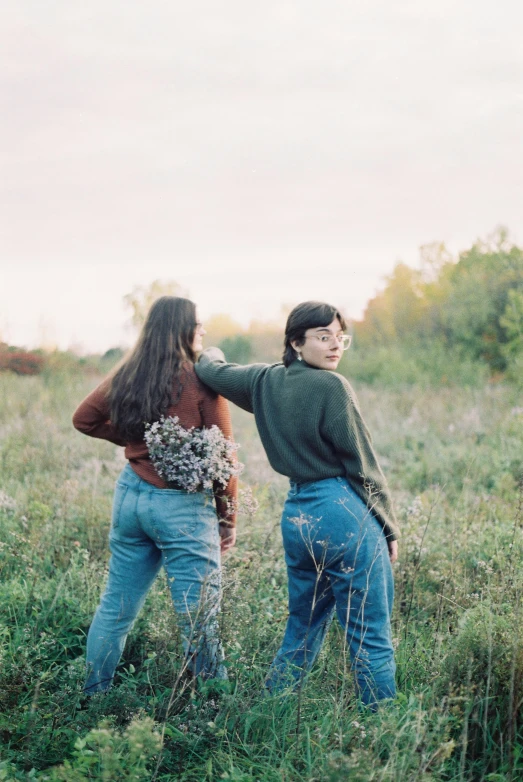 two men standing in tall grass holding onto the backs of their bodies