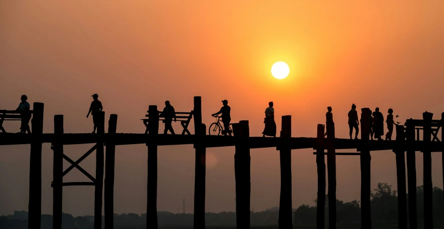 a group of people walking across a bridge with a sunset in the background