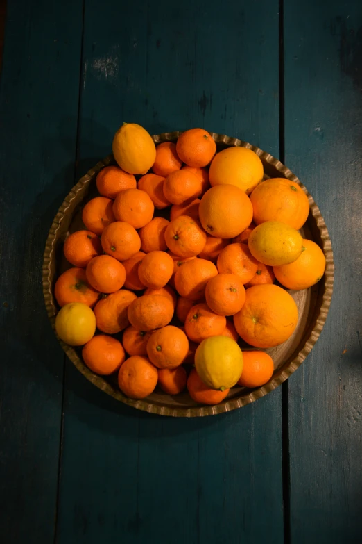 some oranges in a bowl on a wooden table