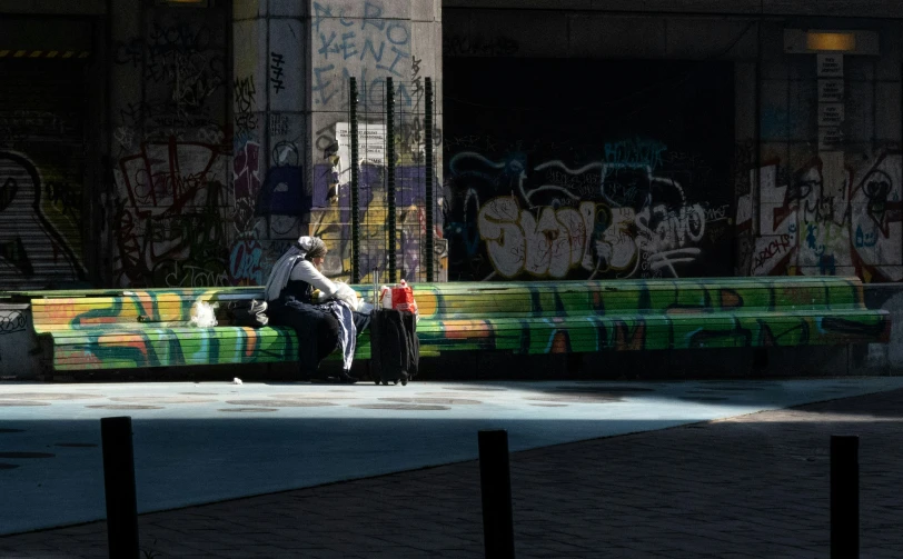 the man sits on the bench near the wall has graffiti