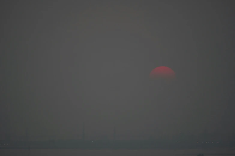 dark gray fog hangs over an ocean with a large sun setting in the distance