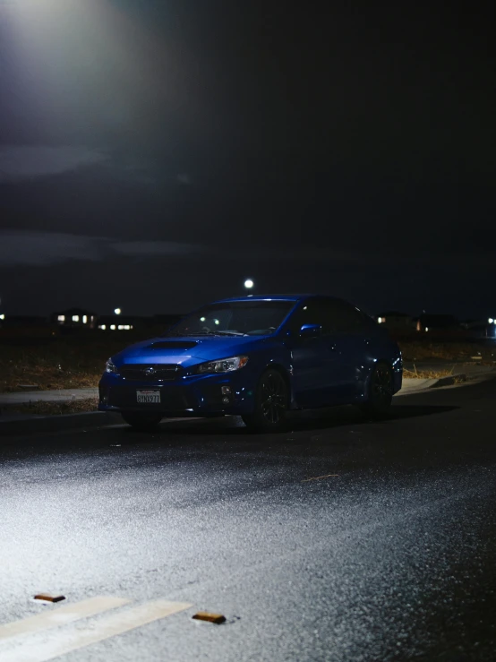 a blue car is driving down the road at night