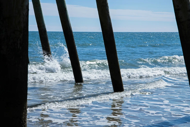 an ocean scene with water, waves and some wooden poles