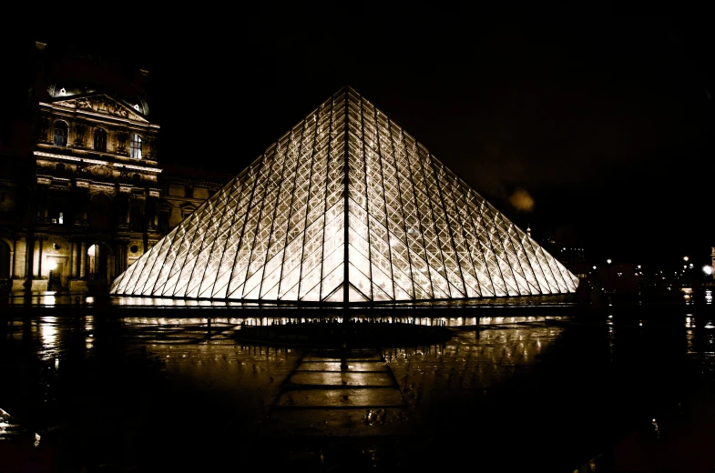 a pyramid lit up in the night in front of a building