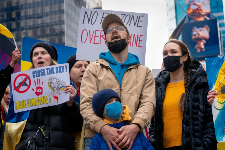 a man in a hat, blue shirt and face mask with other protesters holding placards