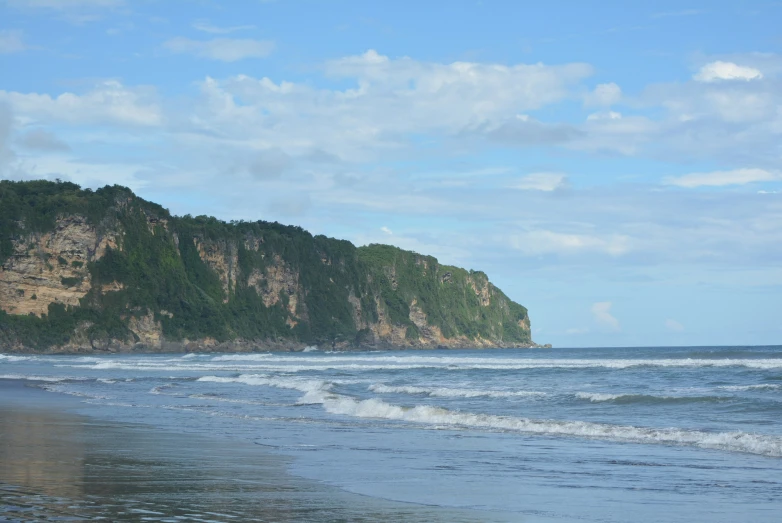 a wave crashes onto the beach near a mountain