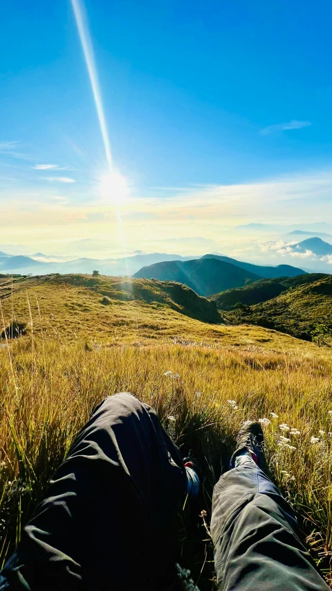 two people are laying on the grass of a hill with mountains in the distance