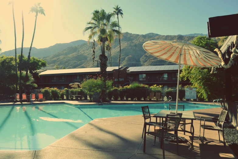 a swimming pool with a patio, tables, chairs and an umbrella over it