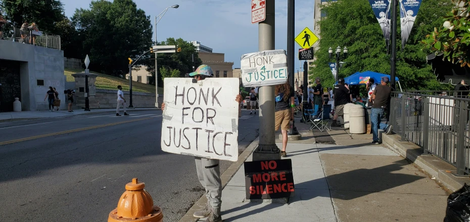 several protestors are standing near the sidewalk holding signs