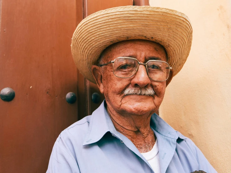 a man wearing a straw hat standing next to a brown door