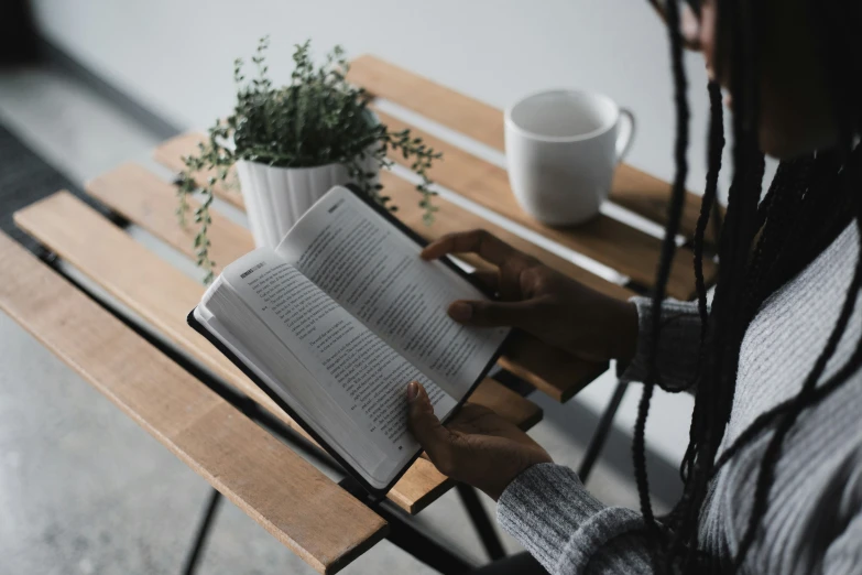 a person reading a book on top of a wooden bench