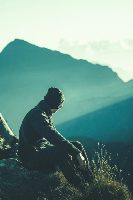 a man sitting on top of a cliff overlooking mountains