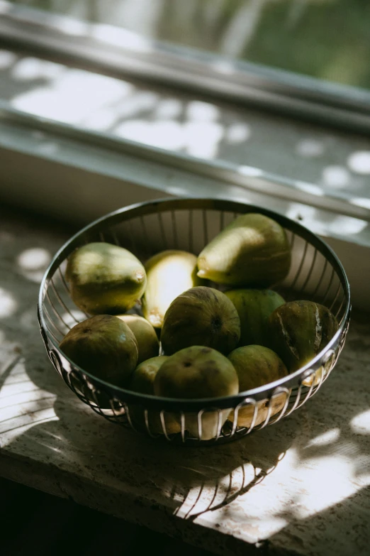 a bowl of green apples in front of a window