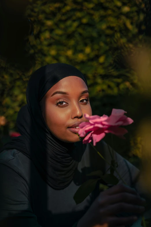 a woman in hijab holds a rose for her face