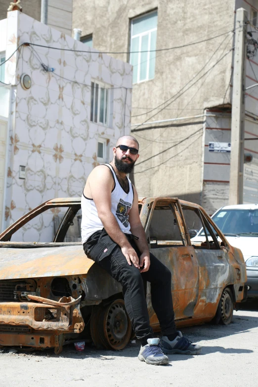 a man sitting on the hood of a car in front of a rusty building