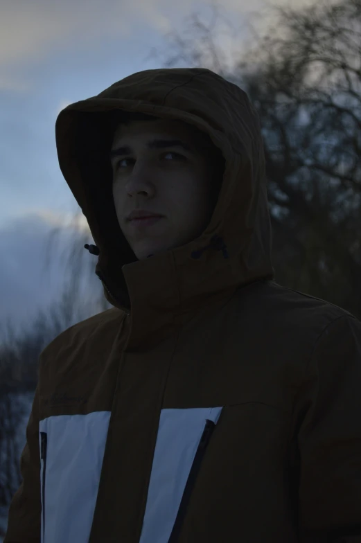 a young man wearing a hooded jacket looks into the distance