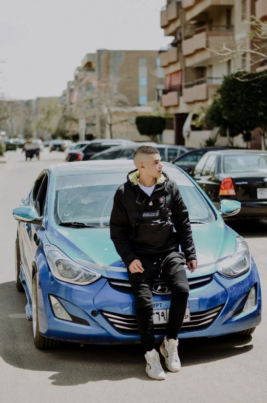 a man sitting on the hood of a blue car