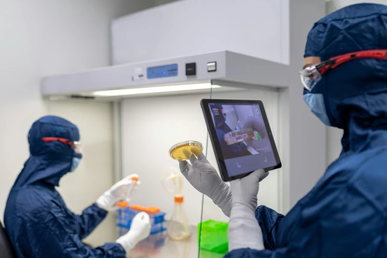 three medical personnel in protective clothing and gloves observe soing on a digital screen