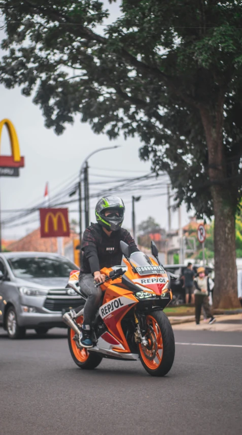 a motorcyclist riding his orange motorcycle past a mcdonald's restaurant