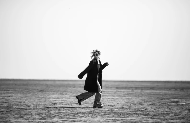 a woman in a black dress and scarf is walking along the beach