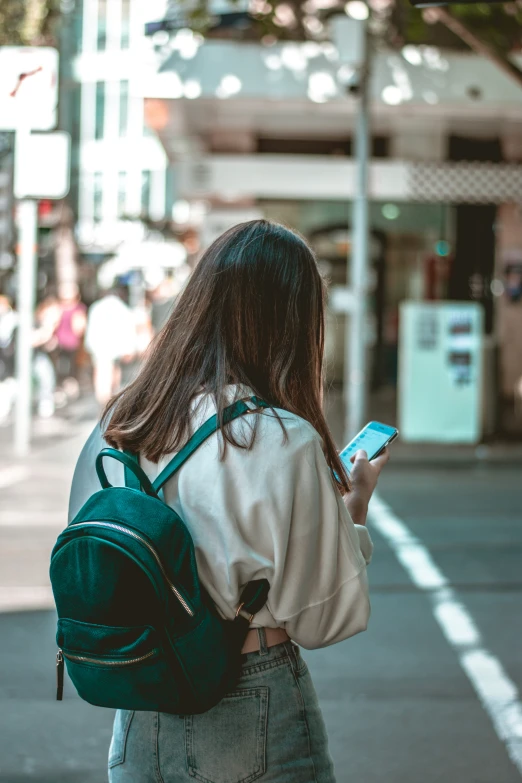 a woman looking at her cell phone and wearing a green backpack