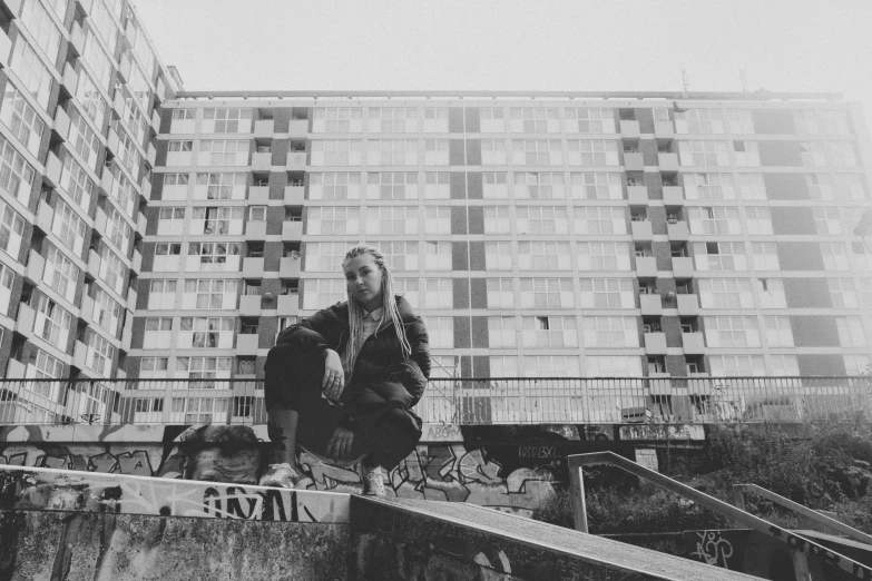 a woman sits on a skateboard outside some apartment buildings