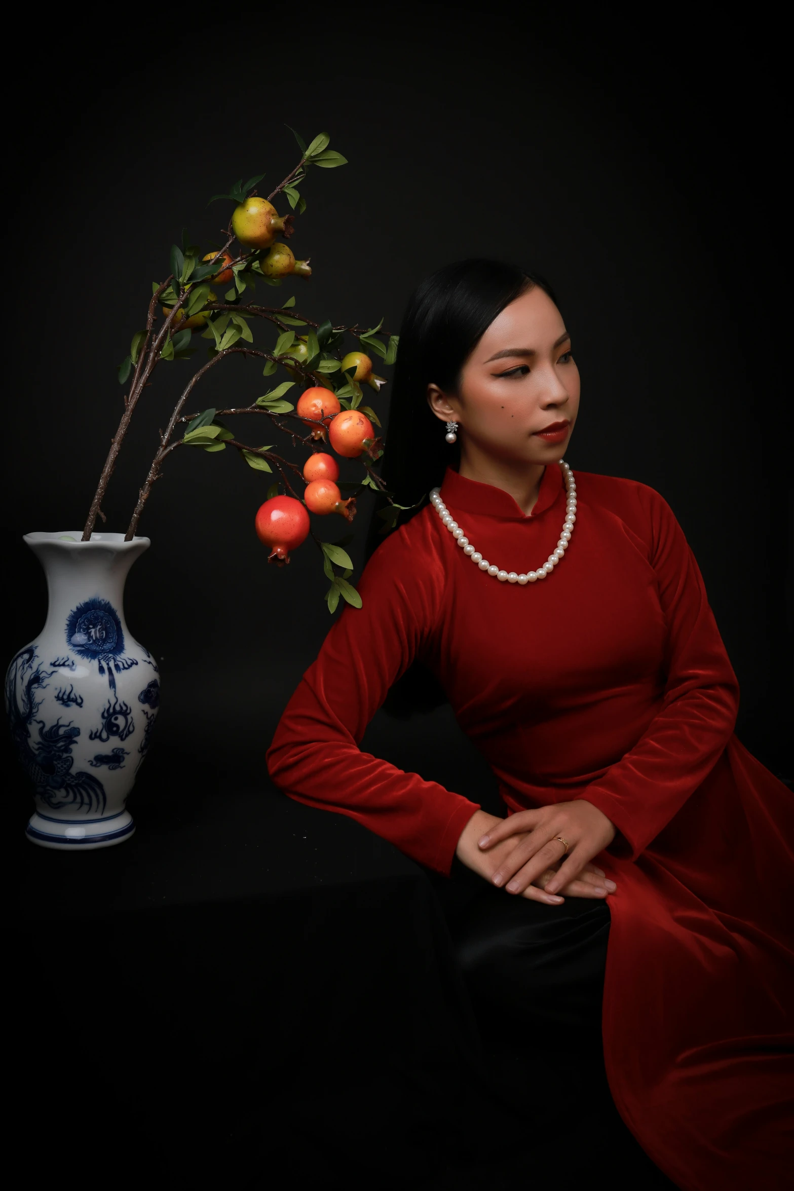 the woman in red is sitting in front of a vase with oranges