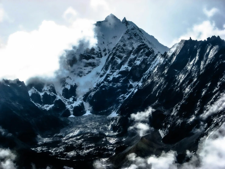 some very snowy mountains with some clouds flying over them