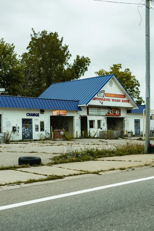 the empty street has a store with blue roof and a red car